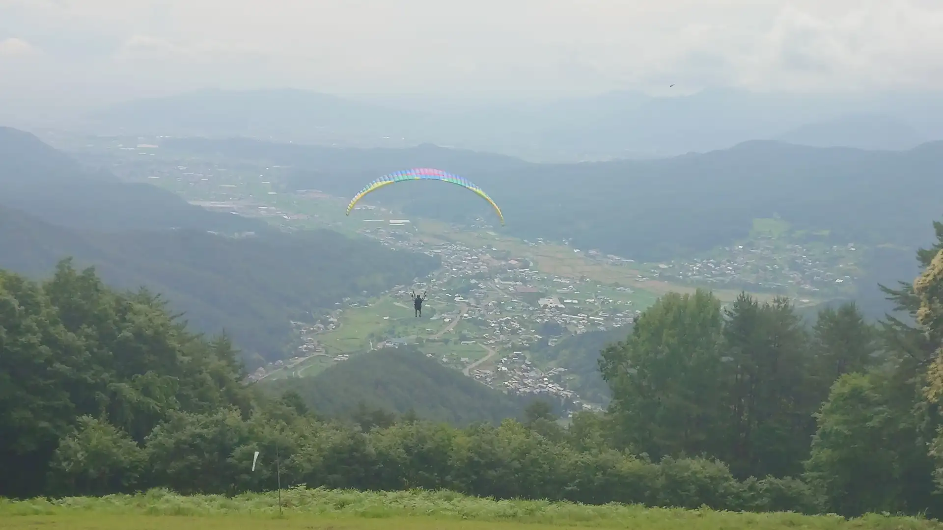 青木村の町並みを背景に空中を進むパラグライダー
