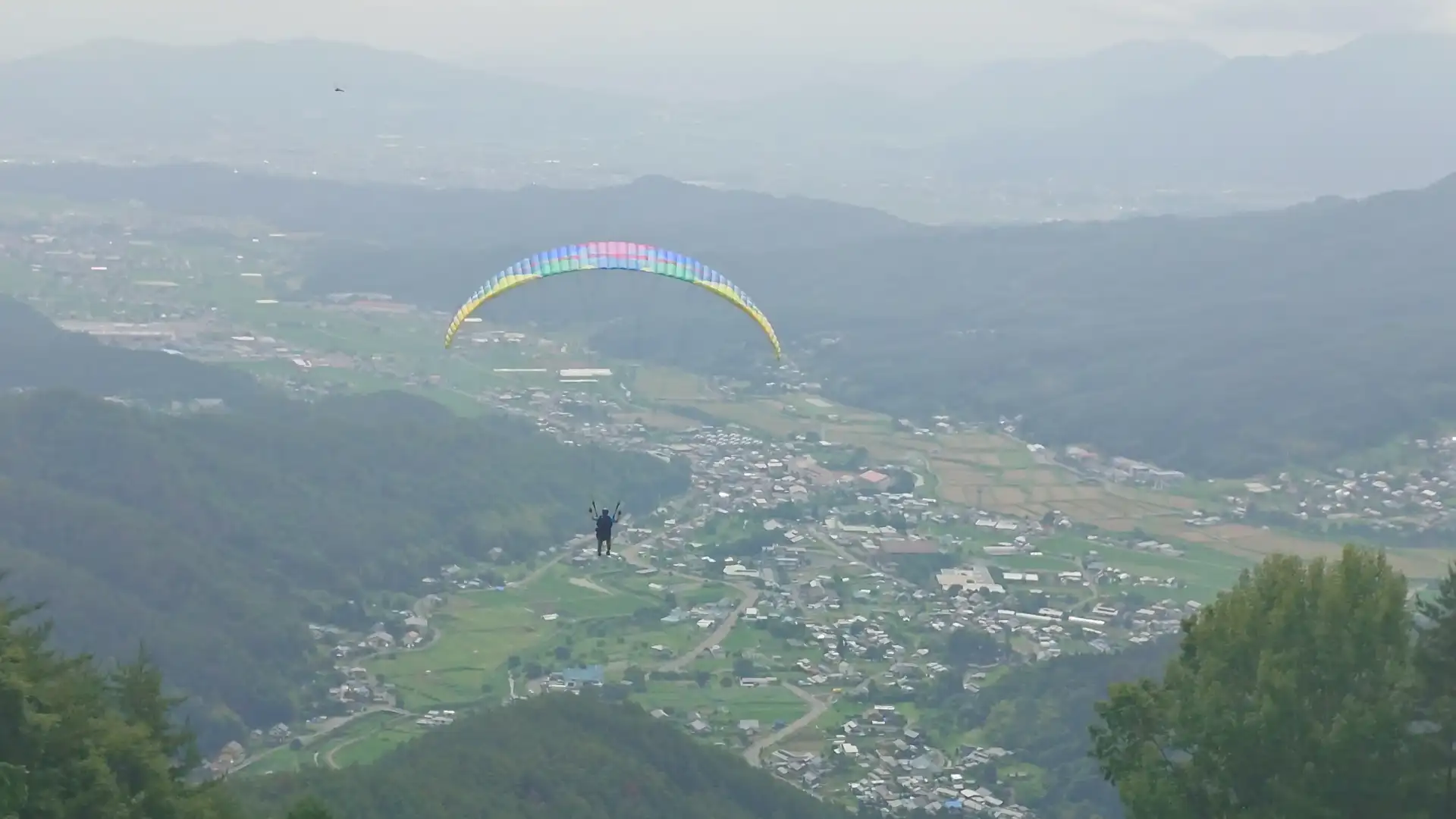 青木村の雄大な景色の中を飛ぶカラフルなパラグライダー