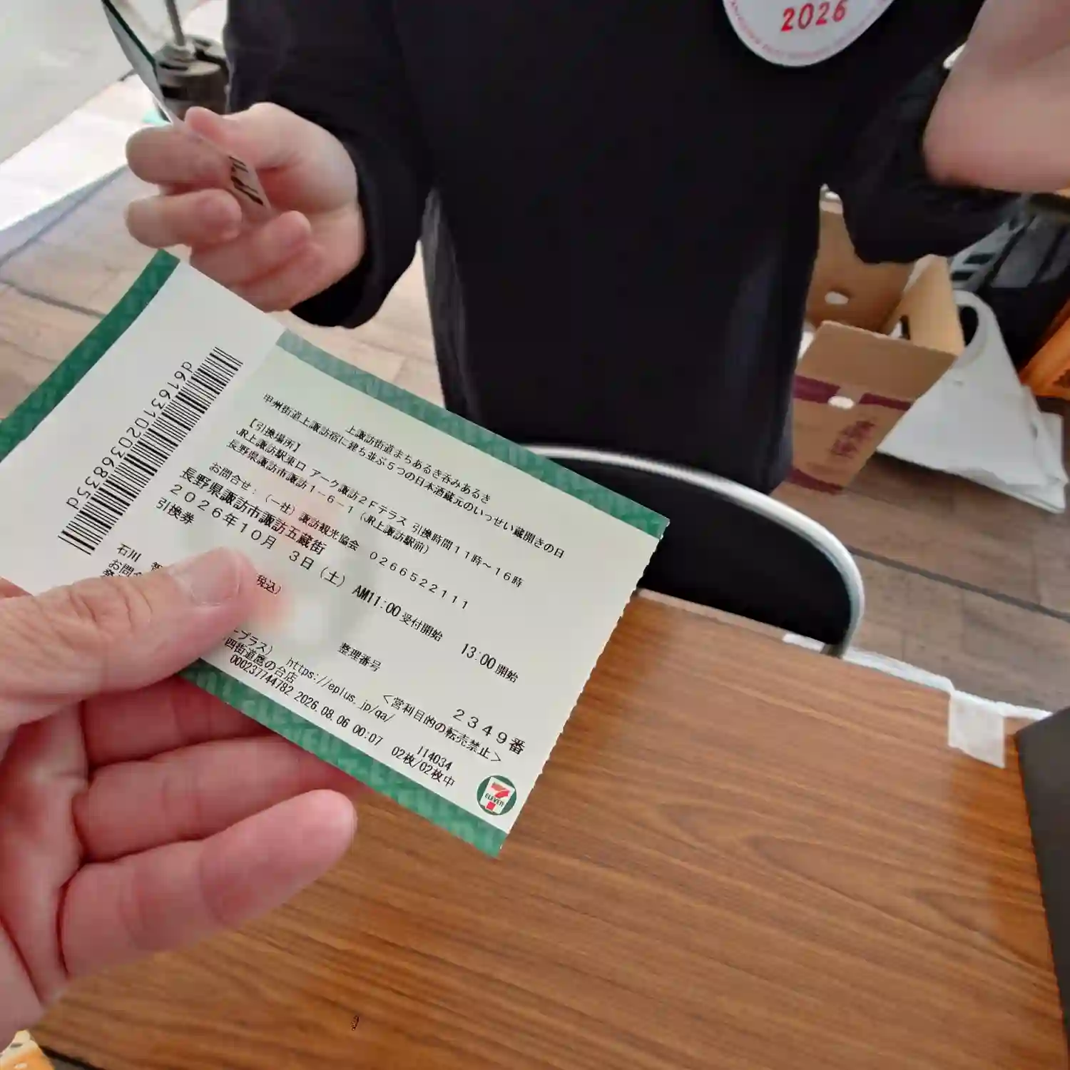 アーク諏訪で上諏訪街道まちあるき呑みあるき2026の受付券を提示する場面